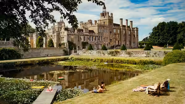people relaxing on the grass and in the water near a large castle
