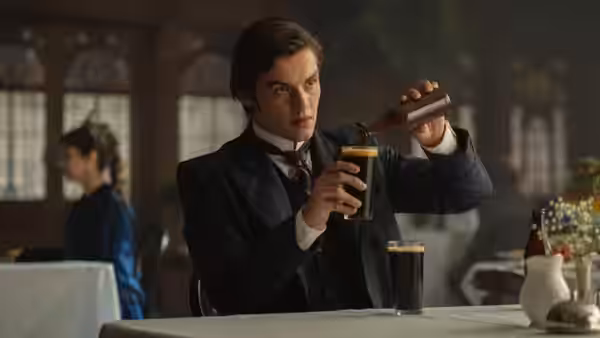 A man in a dark suit pours stout into a glass at a table