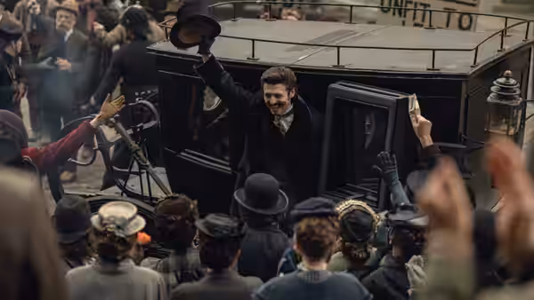 A man waves from a carriage as a crowd cheers around him