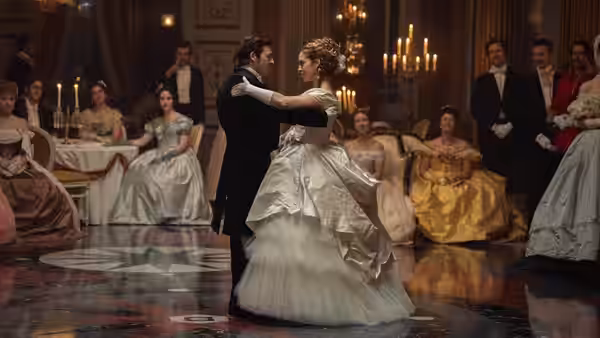 A couple in formal attire dancing in a grand ballroom filled with guests