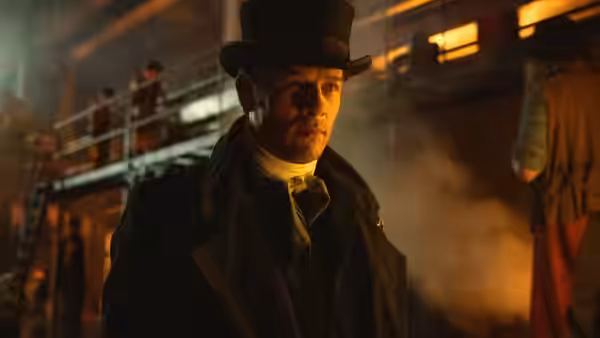 A man in a top hat stands in a dimly lit industrial interior