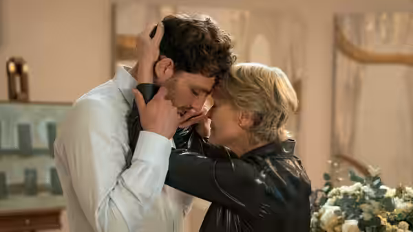 Blonde woman in leather jacket embracing curly-haired man in white shirt