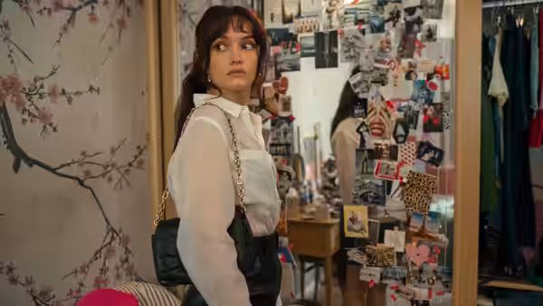 Woman in white shirt and black skirt looking back in cluttered room