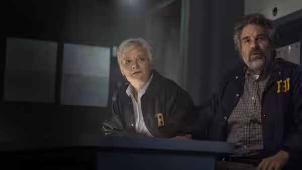Two agents in FBI jackets sitting at a table in a dark room