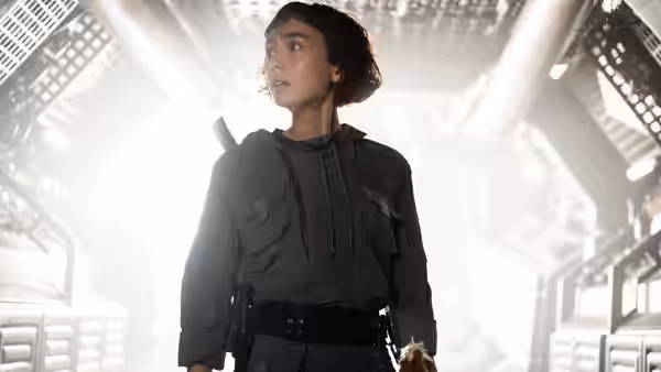 Wendy (Sydney Chandler) standing alert in a brightly lit industrial corridor