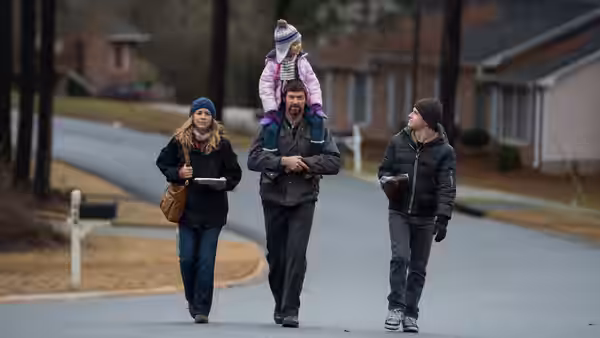 Keller Dover (Hugh Jackman) with daughter on shoulders walking with two women on a suburban road