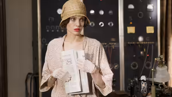 Christine Collins holds a newspaper in front of a bank of control panels
