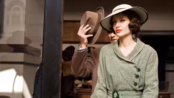 Christine Collins stands outside a doorway as a man raises his hat