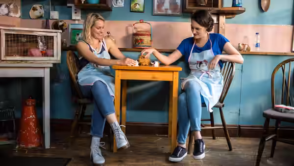 Fleabag (Phoebe Waller-Bridge) and Boo sit at a table holding a guinea pig