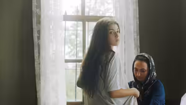 Girl standing by window as woman kneels beside her