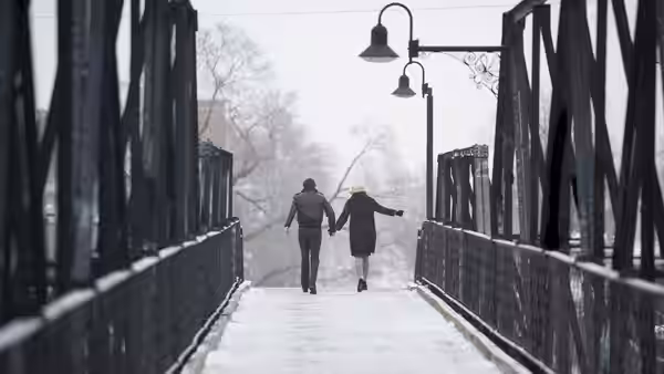 a couple holding hands while walking across a snow-covered bridge