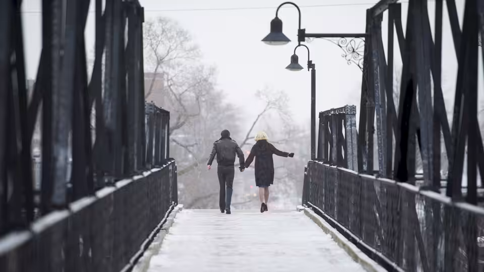 a couple holding hands while walking across a snow-covered bridge