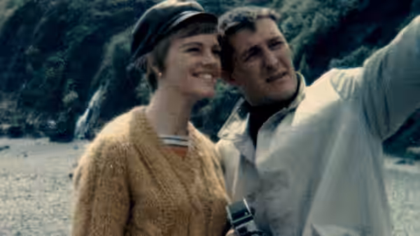 a smiling couple standing on a rocky beach with a camera