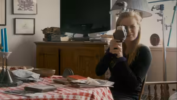 Woman holding a vintage camera while seated at a table indoors
