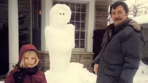 a man and young girl beside a large snowman outdoors