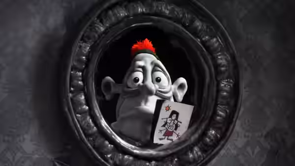 A clay figure with a red hair tuft peers through a round frame holding a card