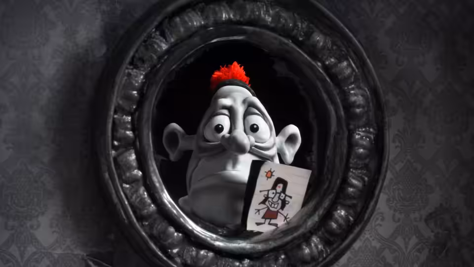 A clay figure with a red hair tuft peers through a round frame holding a card