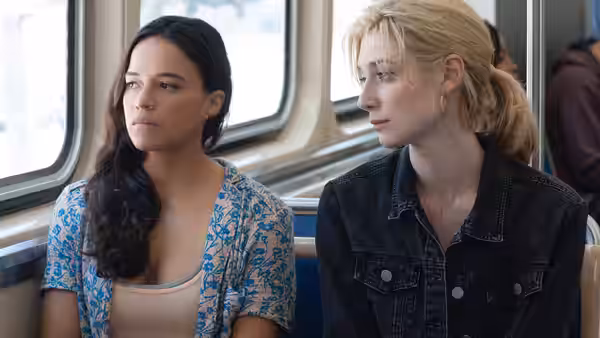 Michelle Rodriguez and Elizabeth Debicki seated together on a train