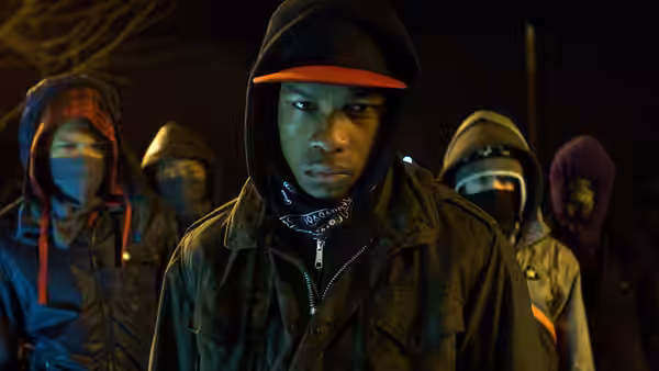 Moses (John Boyega) stands in front of several masked youths at night