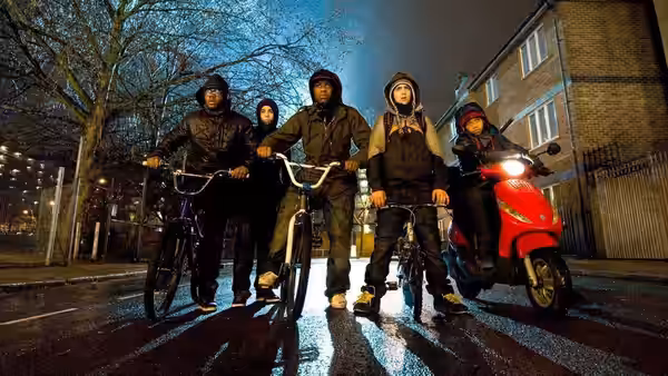 Four youths stand with bicycles and a red scooter on a wet street at night