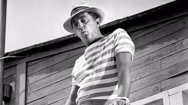 Max Cady (Robert Mitchum) looks down from beside a wooden waterfront building