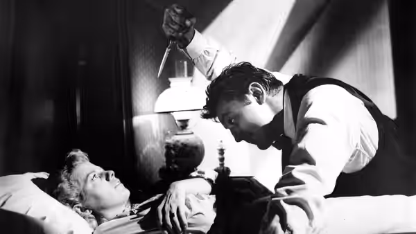 Preacher Harry Powell (Robert Mitchum) holding a knife over Willa Harper (Shelley Winters) in bed