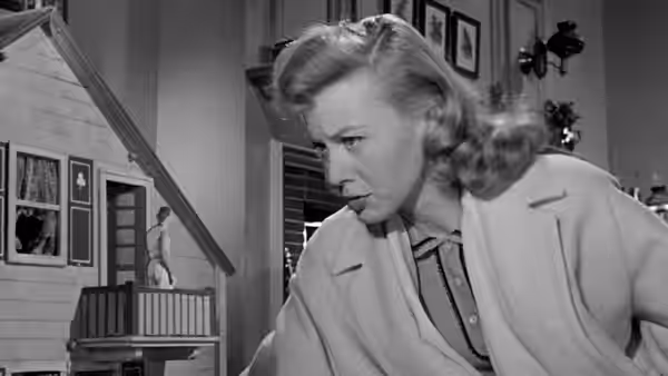 Louise Carey (Randy Stuart) leans over a miniature house, looking down
