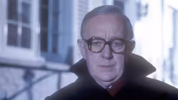 George Smiley (Alec Guinness) in glasses and dark coat looking ahead