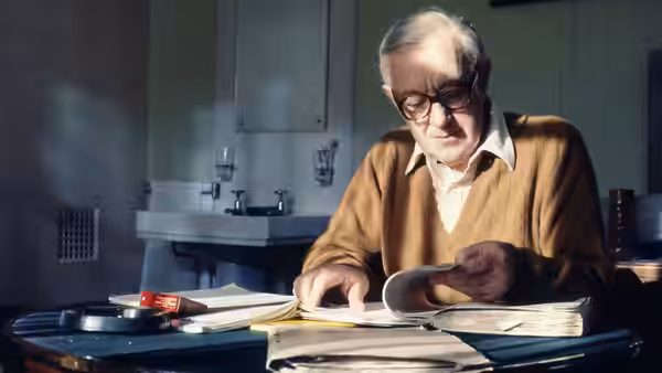 George Smiley (Alec Guinness) reading papers at a desk in an office