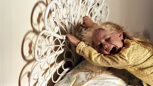 Carol Anne Freeling (Heather O'Rourke) screams while gripping a white metal bed frame