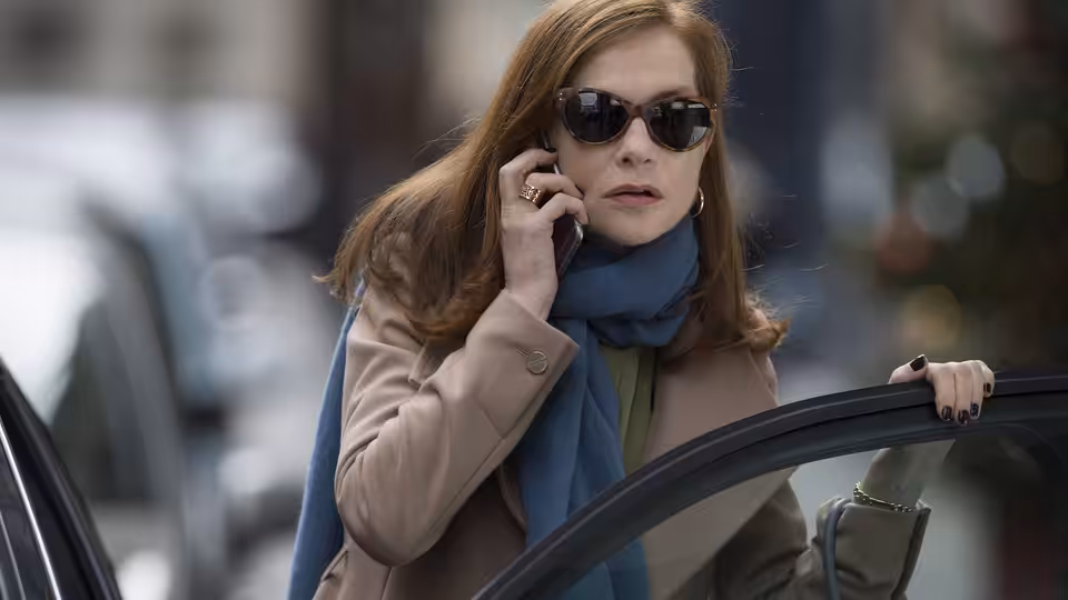 Michèle (Isabelle Huppert) speaking on a phone beside an open car door