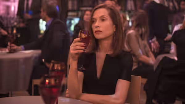 Michèle (Isabelle Huppert) holding a glass of red wine in a restaurant