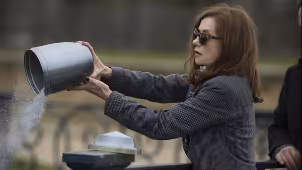 Michèle (Isabelle Huppert) pouring powder from a metal container outdoors