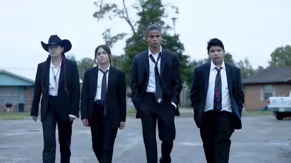 Four people in dark suits walking across an empty lot