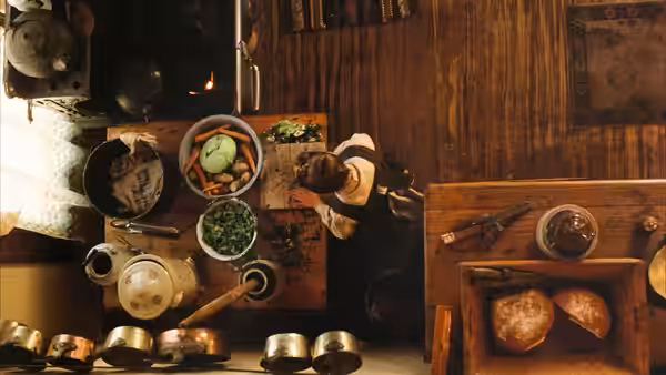 Woman chops vegetables at cluttered wooden table in dim kitchen