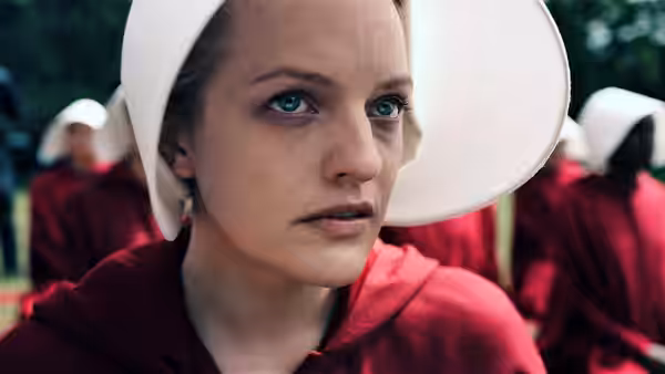 June Osborne (Elisabeth Moss) in close-up with handmaids visible behind her