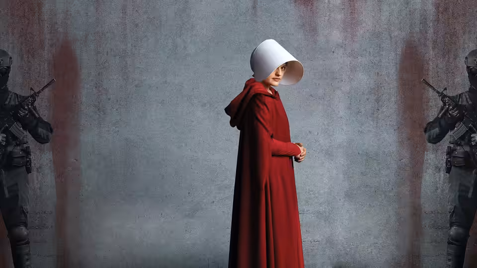 Offred (Elisabeth Moss) standing between two armed guards before a blood-stained wall