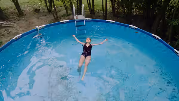 Jay Height (Maika Monroe) floating with arms outstretched in an above-ground pool