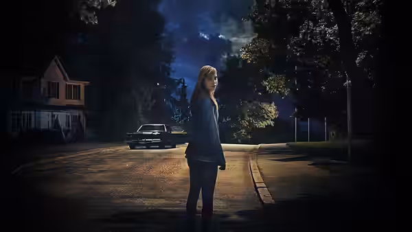 Jay Height (Maika Monroe) standing alone on a quiet suburban street at night