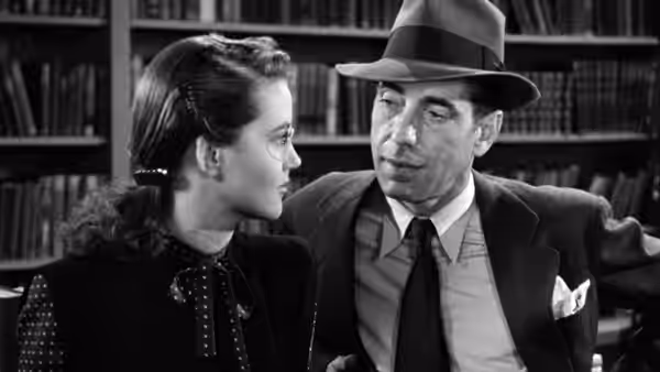 Philip Marlowe (Humphrey Bogart) speaks with a woman wearing glasses in front of bookshelves