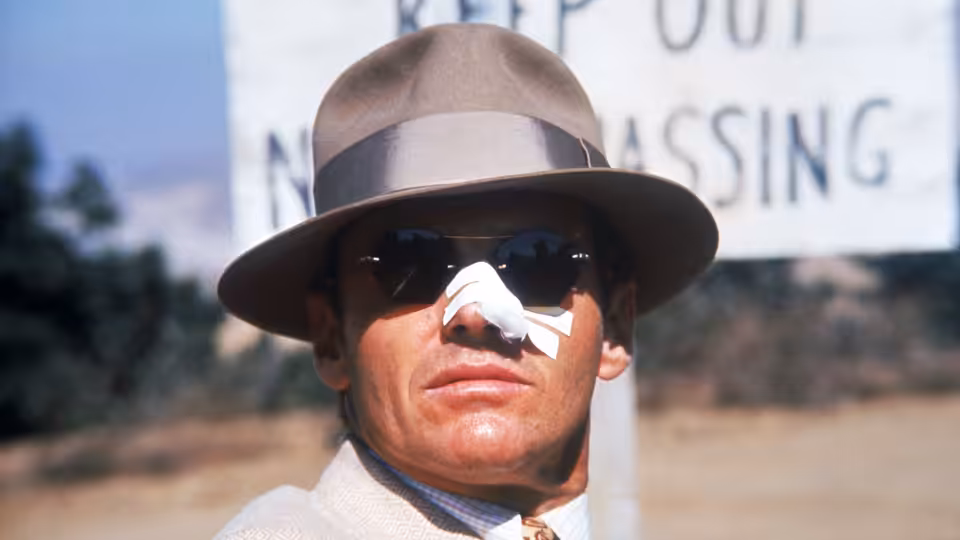 Jake Gittes (Jack Nicholson) wearing a fedora and nose bandage outdoors