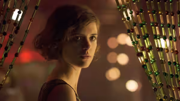 Young woman with bobbed hair looks back through a beaded curtain