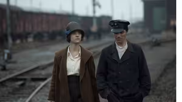 Woman in hat and coat stands with a man on railway tracks