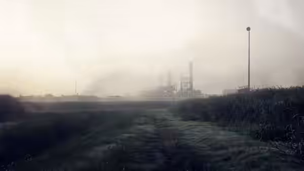 an abandoned industrial plant visible through fog from a dirt path in grass