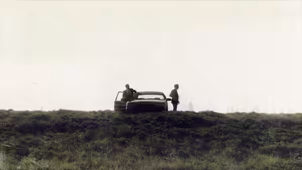 two men next to a car parked on a hill under a hazy sky