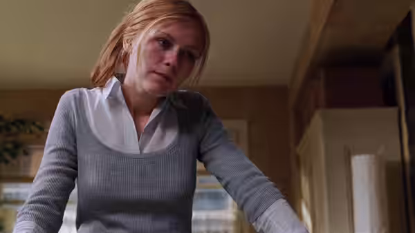 A blonde woman leans forward in a room, looking down with concern