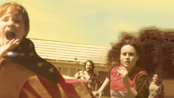 A boy wrapped in an American flag shouting as a woman runs past a house