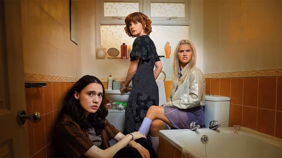 Josie (Kat Sadler) sits on the bathroom floor while Deb (Louise Brealey) stands and Billie (Lizzie Davidson) perches on the toilet