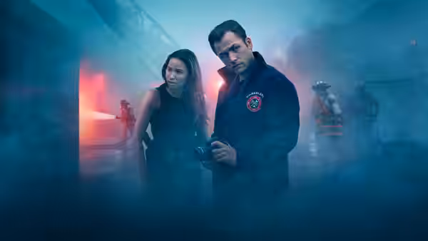 Dave Gudsen (Taron Egerton) holds a camera beside Michelle Calderone (Jurnee Smollett-Bell) in a smoky hallway