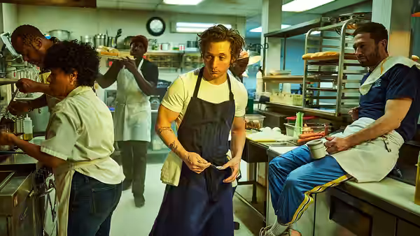 Carmy (Jeremy Allen White) adjusts his apron in a busy kitchen as staff work around him